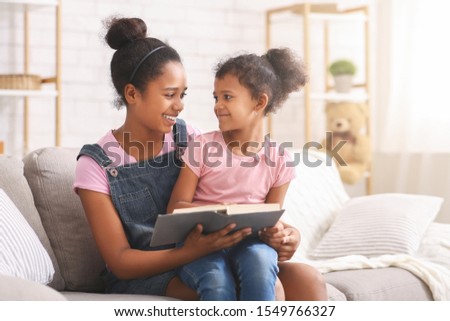 Story time. African teen sister reading book to her little sister, free space