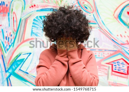 young pretty afro woman feeling sad, frustrated, nervous and depressed, covering face with both hands, crying against graffiti wall