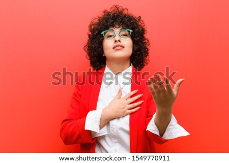 young pretty afro woman feeling happy and in love, smiling with one hand next to heart and the other stretched up front