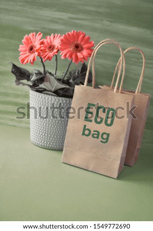 Coral gerbera daisy flowers and craft papper shopping bags on green paper background. Springtime sustainable lifestyle concept image with text "Eco bag" on the craft paper bag.