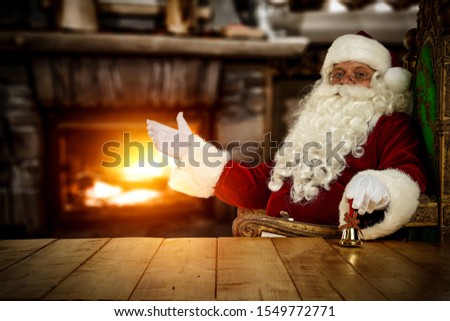 Red old santa claus in red clothes.Wooden table with free space for your decoration.Home interior with fireplace and warm mood light.Chrsitmas time and cold winter night.Copy space.Old Noel on chair. 