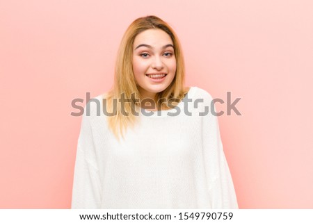 young pretty blonde woman looking happy and goofy with a broad, fun, loony smile and eyes wide open against pink flat wall
