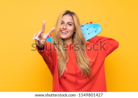 Young skater woman making victory gesture over isolated yellow background
