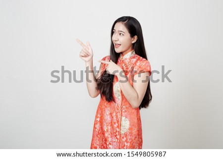 Woman pointing to blank space, Beautiful Asian woman wearing red Chinese traditional dress smiling  on gray banner background with copy space for concept Happy chinese new year