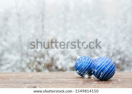 Beautiful Christmas bauble decorations lie on the wooden table over snow covered forest background.