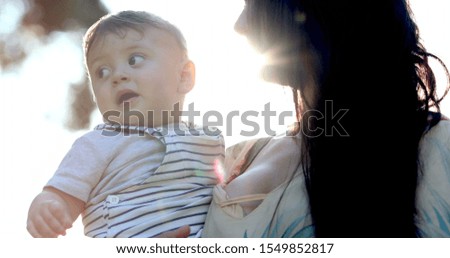 Mother holding baby toddler son outside in the sunlight lens-flare