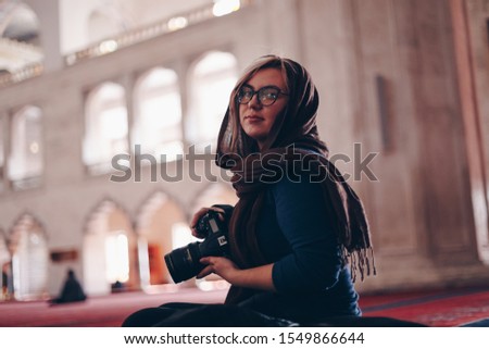 portrait of a beautiful blonde tourist woman visiting and taking photos of kocatepe mosque in ankara, turkey. concept of travelling and experiencing new religions and cultures