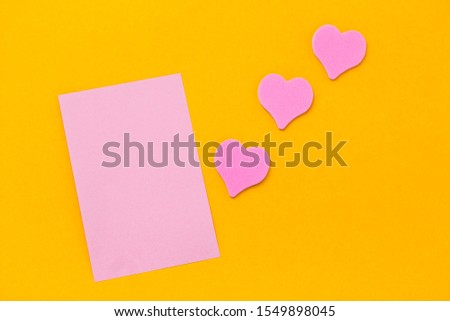 pink blank paper sheet and pink hearts on a yellow background copy space