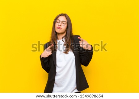 young  pretty woman with a bad attitude looking proud and aggressive, pointing upwards or making fun sign with hands against orange wall