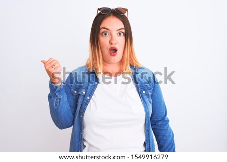 Beautiful woman wearing denim shirt standing over isolated white background Surprised pointing with hand finger to the side, open mouth amazed expression.