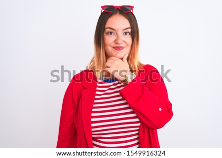 Young beautiful woman wearing striped t-shirt and jacket over isolated white background looking confident at the camera with smile with crossed arms and hand raised on chin. Thinking positive.