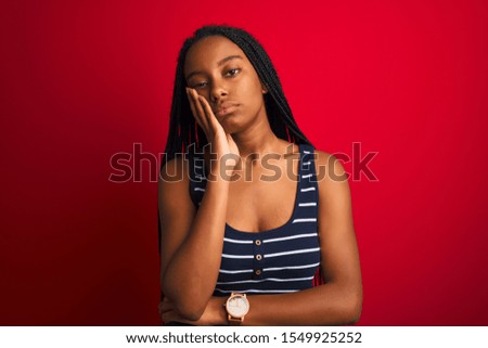 Young african american woman wearing striped t-shirt standing over isolated red background thinking looking tired and bored with depression problems with crossed arms.