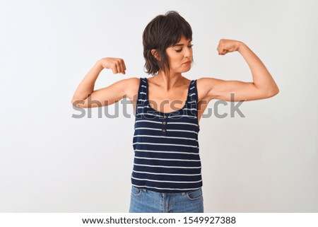 Young beautiful woman wearing striped t-shirt standing over isolated white background showing arms muscles smiling proud. Fitness concept.