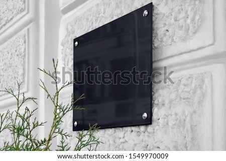 Blank black glass signboard on gray textured wall mockup. Empty hanging plexiglas nameplate mock up. Clear dark namesign on wal for corporate or store title mokcup template.