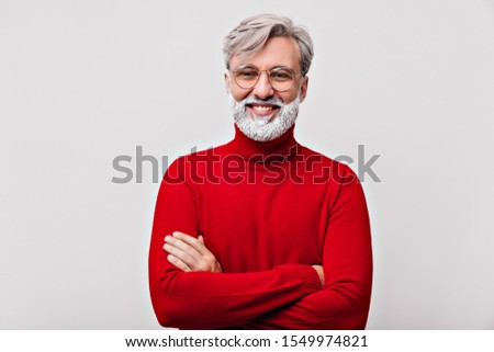 Studio shot of good-humoured grandfather with sincere smile. Portrait of caucasian old man standing with arms crossed.