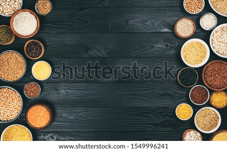 Frame of various cereals, grains, seeds and beans, high fibre diet concept, porridge collection on black wooden background with copy space, photo filtered in vintage style, top view