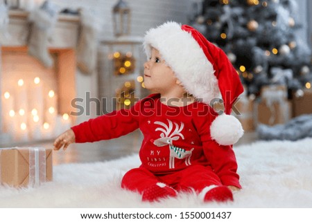 Little baby with Santa hat and Christmas gift on floor at home