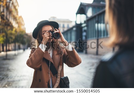 Outdoor smiling lifestyle portrait of pretty young woman having fun in sun city Europe autumn with camera travel photo of photographer Making pictures in glasses and hat with girlfriends