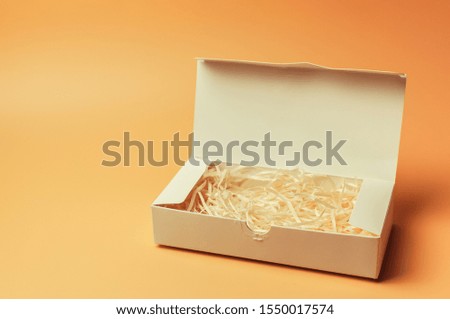 Open gift white box inside with paper hay on a beige background, isolate. Copyspace. The concept of sales, discounts, Christmas gifts and shopping.
