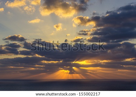 Sun rays emerging through the clouds at sunset sunrise at sea