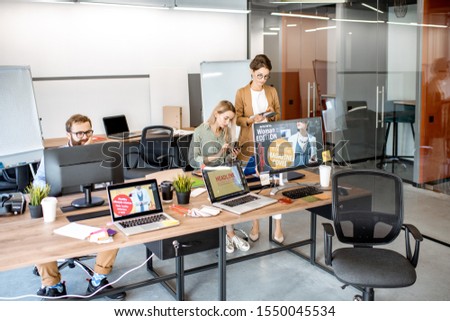 Modern office room of web designers with working places and people working