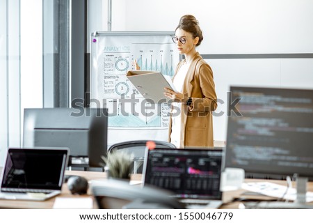 Young business woman preparing for a presentation, standing alone with documents near flipchart in the modern office or coworking space Royalty-Free Stock Photo #1550046779