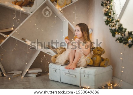 Little girl sitting in a room decorated with New Year's decor. Girl holding gingerbread cookies.