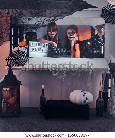 Two pensive girls with scary makeup are sitting next to traditionally decorated table.