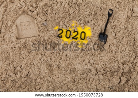 The New Year 2020 concept dug into the sand with a shovel, next to the house imprinted on the sand