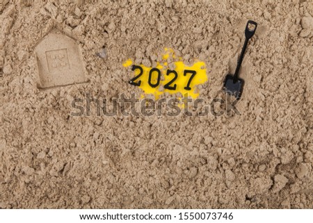 The New Year 2027 concept dug into the sand with a shovel, next to the house imprinted on the sand