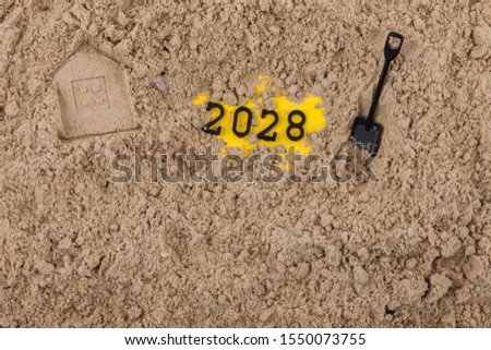 The New Year 2028 concept dug into the sand with a shovel, next to the house imprinted on the sand