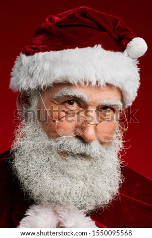 Head and shoulders portrait of fairytale Santa Claus looking at camera kindly while posing against red background