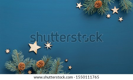 Flat lay Christmas tree branches with cones and wooden vintage stars over blue background. Top view. Xmas banner mockup with copy space, greeting card template.