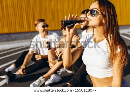 Young friends, men and women having fun in the city, sitting on the road with drinks in hand