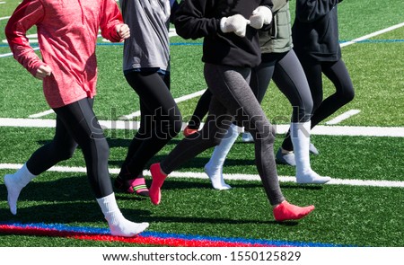 A high school running team is running together wearing spandex and socks with long sleeves due to cold weather. Royalty-Free Stock Photo #1550125829