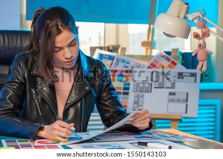Girl in a leather jacket sitting at a Desk in the office. The work of the designer of mobile applications. The girl is developing a project of the user interface of the program. UI. UX