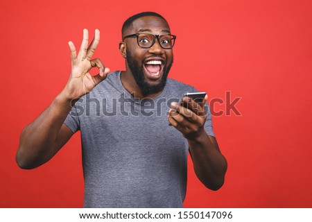 Afro american man using smartphone over isolated red background doing ok sign with fingers, excellent symbol.
