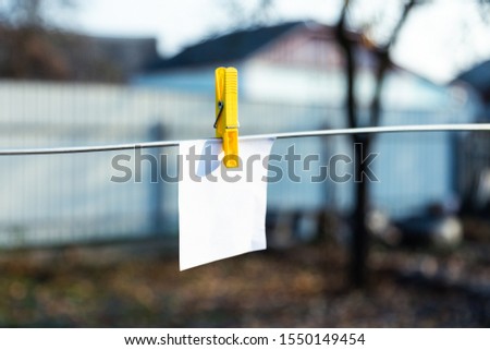 A white sheet of paper attached by a yellow clothespin hangs on the street on a clothesline. Empty space for text