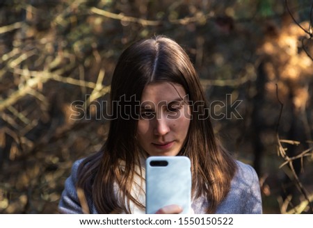 Girl in a gray coat takes a selfie in the forest. Outdoor communication mobile phone.