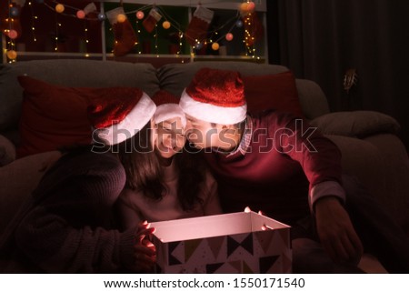 happy family, father mother kiss daughter during open a gift present box together at christmas day night in living room that decorated with christmas tree for christmas festival day