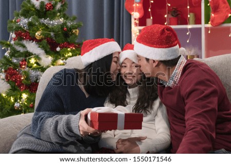 happy family, father mother give gift present and kiss daughter, they celebrate together at christmas day night in living room that decorated with christmas tree for christmas festival day