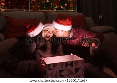 happy family, father mother kiss daughter during open a gift present box together at christmas day night in living room that decorated with christmas tree for christmas festival day