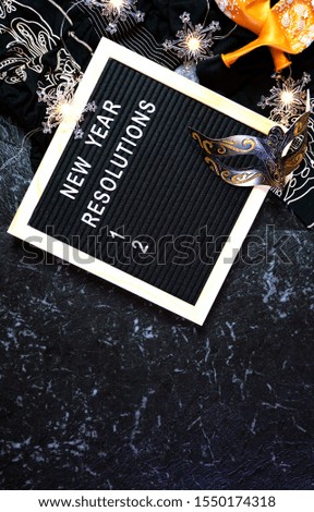 New Year's Eve resolutions flatlay with letter board and black and gold party decorations with negative copy space.