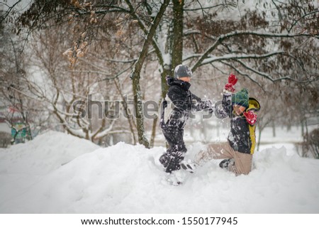 Two boys play on pile of snow after heavy snowfall in city. Children on a walk in park in winter. Active healthy lifestyle.