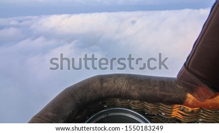 Adventure first person view, pov from basket of field, meadow, river and above cloud in flight on hot air balloon. The aircraft fly in morning blue sky. Hot air balloon burner flame into envelope.