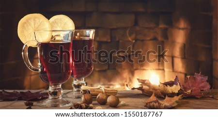 Two glasses of mulled wine on a wooden table in front of a burning fireplace, horizontal banner, copy space.