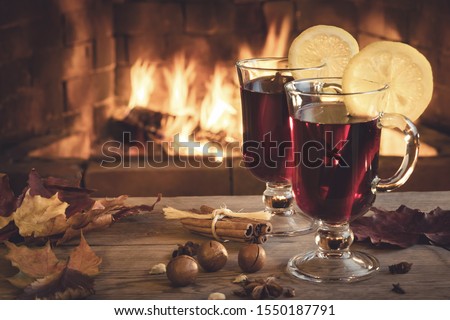 Two glasses of mulled wine on a wooden table in front of a burning fireplace.