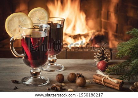 Two glasses of mulled wine on a wooden table near a Christmas tree in front of a burning fireplace.