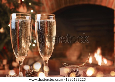 Two glasses with champagne on a wooden table in a room with a burning fireplace.
