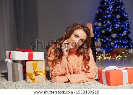 Portrait of a beautiful woman with curls at the Christmas tree with gifts of new year lights garland